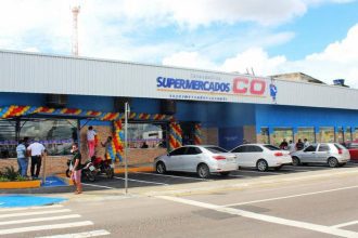 Fachada do Supermercado C.O com carros estacionados e pessoas na entrada.