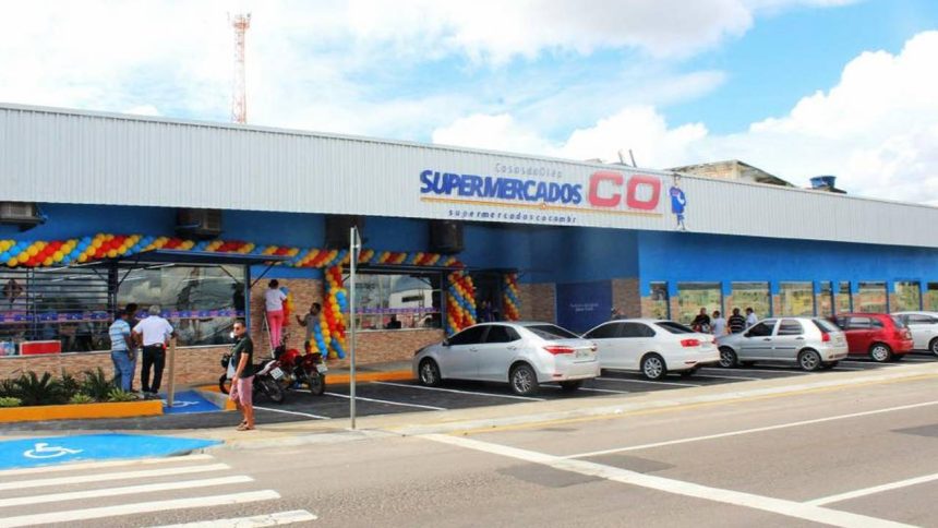 Fachada do Supermercado C.O com carros estacionados e pessoas na entrada.