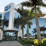 Fachada moderna da EMS, farmacêutica, com palmeiras e céu azul.