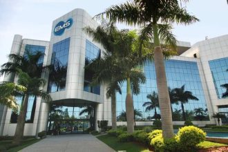 Fachada moderna da EMS, farmacêutica, com palmeiras e céu azul.