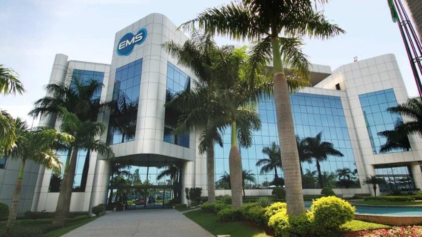 Fachada moderna da EMS, farmacêutica, com palmeiras e céu azul.