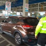 Fiscal de trânsito em vaga para PcD ao lado de carro marrom em estacionamento.