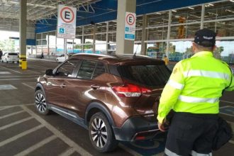 Fiscal de trânsito em vaga para PcD ao lado de carro marrom em estacionamento.