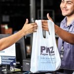 Funcionário entregando sacola com logo PMZ, Peças e Pneus, em loja