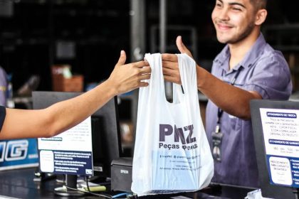 Funcionário entregando sacola com logo PMZ, Peças e Pneus, em loja