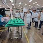 Funcionários em fábrica no Polo Industrial de Manaus, observando processo.