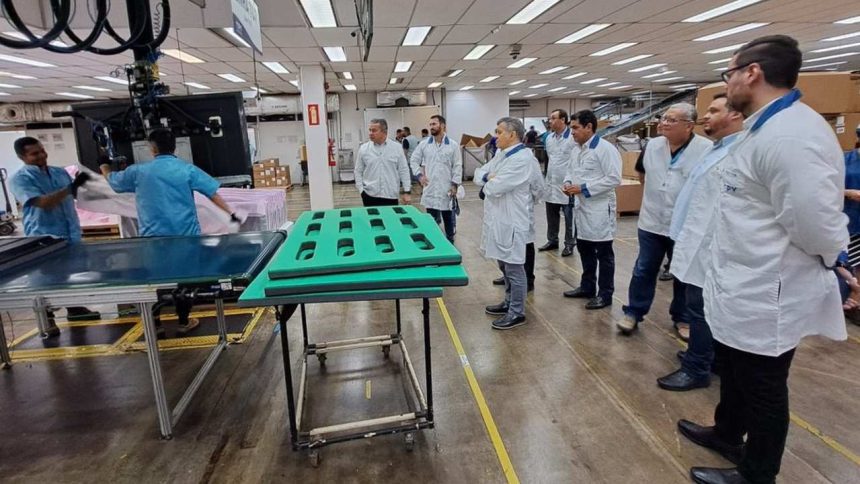 Funcionários em fábrica no Polo Industrial de Manaus, observando processo.