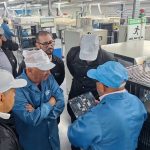 Grupo de pessoas em fábrica observando placa de circuito.