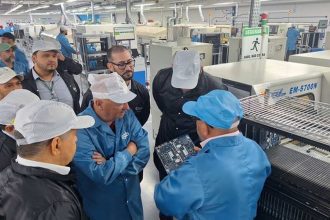 Grupo de pessoas em fábrica observando placa de circuito.
