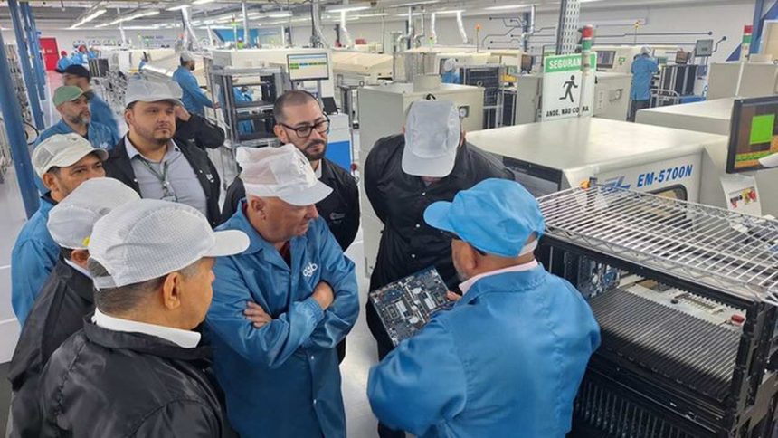 Grupo de pessoas em fábrica observando placa de circuito.