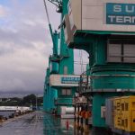 Guindastes de carga no porto com o céu nublado ao fundo. O letreiro diz 'SUPER TERMINAIS'.