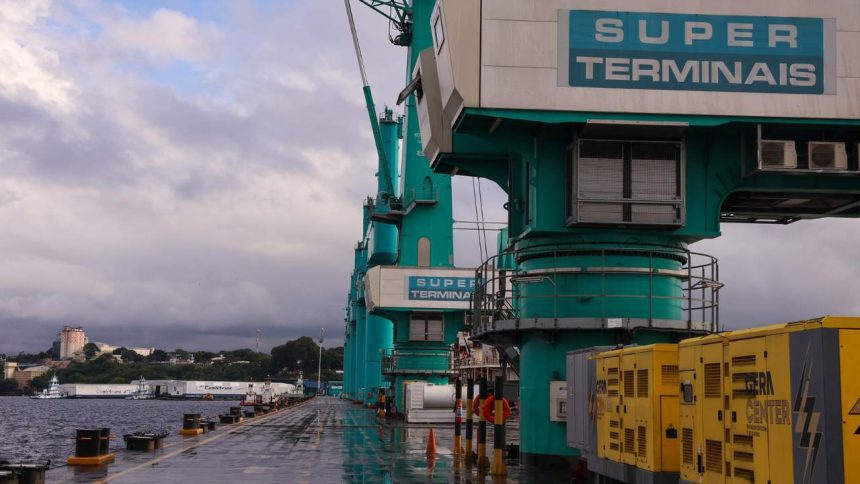 Guindastes de carga no porto com o céu nublado ao fundo. O letreiro diz 'SUPER TERMINAIS'.