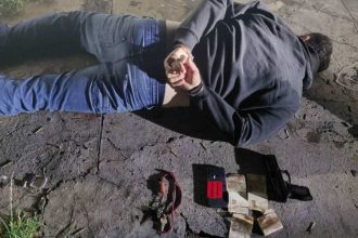 Homem algemado no chão após assalto com arma e celular.