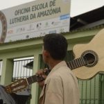 Homem carrega violão em frente a escola de lutheria da Amazônia, a OELA