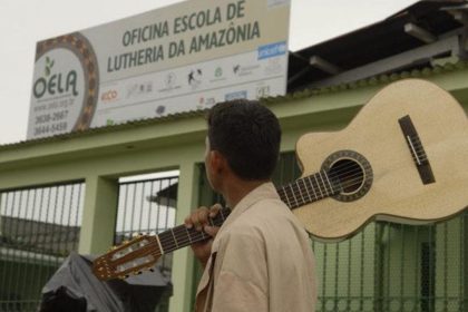 Homem carrega violão em frente a escola de lutheria da Amazônia, a OELA