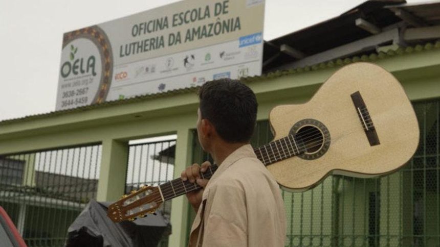 Homem carrega violão em frente a escola de lutheria da Amazônia, a OELA