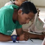 Homem desenhando em papel, com colegas ao redor.