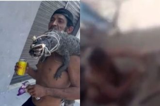 Homem segura jacaré morto nos ombros, com bebida na mão, cena de violência.