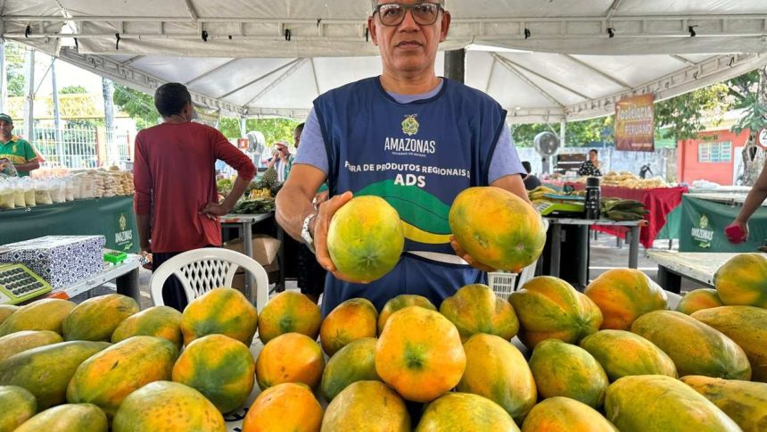 Homem segura mamões maduros em feira de produtos regionais em Manaus.