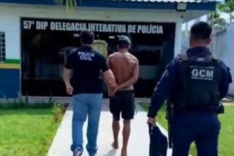 Homem sendo escoltado por policiais em frente à delegacia de polícia.