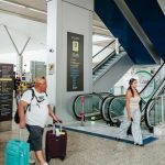 Interior do Aeroporto de Manaus com pessoas caminhando e escadas rolantes.