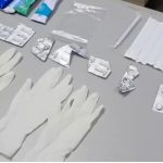 Itens médicos, como luvas, embalagens de remédios e seringas, dispostos sobre uma superfície.