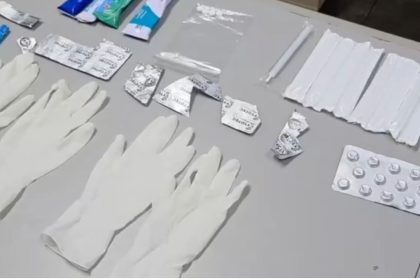 Itens médicos, como luvas, embalagens de remédios e seringas, dispostos sobre uma superfície.