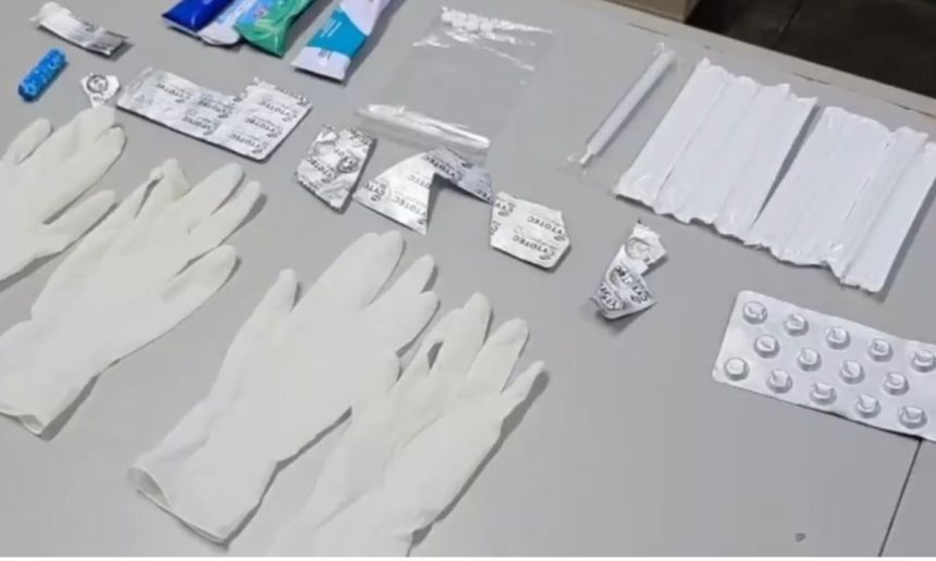 Itens médicos, como luvas, embalagens de remédios e seringas, dispostos sobre uma superfície.