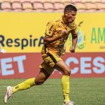 Jogador de futebol comemorando gol em campo, vestindo uniforme amarelo e preto.