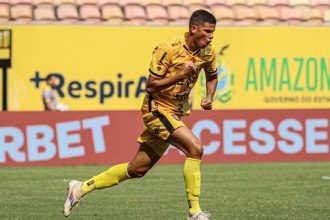 Jogador de futebol comemorando gol em campo, vestindo uniforme amarelo e preto.