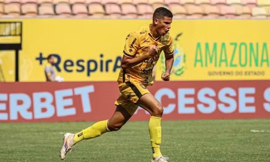 Jogador de futebol comemorando gol em campo, vestindo uniforme amarelo e preto.