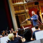 Maestro conduz orquestra durante apresentação no palco de teatro.