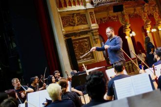 Maestro conduz orquestra durante apresentação no palco de teatro.
