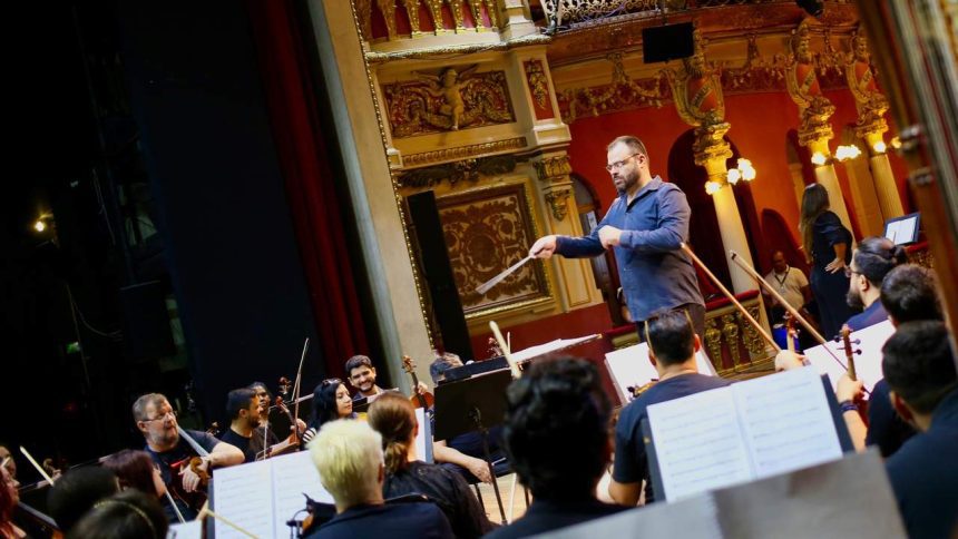 Maestro conduz orquestra durante apresentação no palco de teatro.