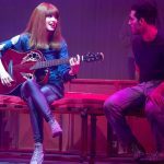 Mel Lisboa como Rita Lee tocando guitarra em espetáculo teatral.