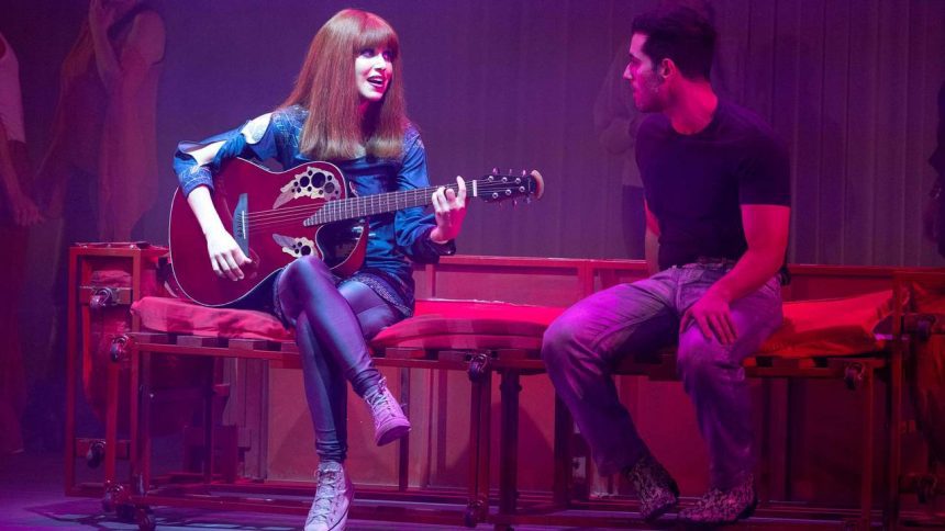 Mel Lisboa como Rita Lee tocando guitarra em espetáculo teatral.