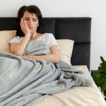 Mulher deitada na cama, aparentemente com problemas de sono, segurando o rosto