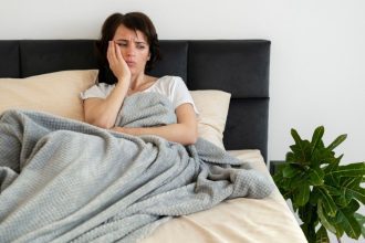 Mulher deitada na cama, aparentemente com problemas de sono, segurando o rosto