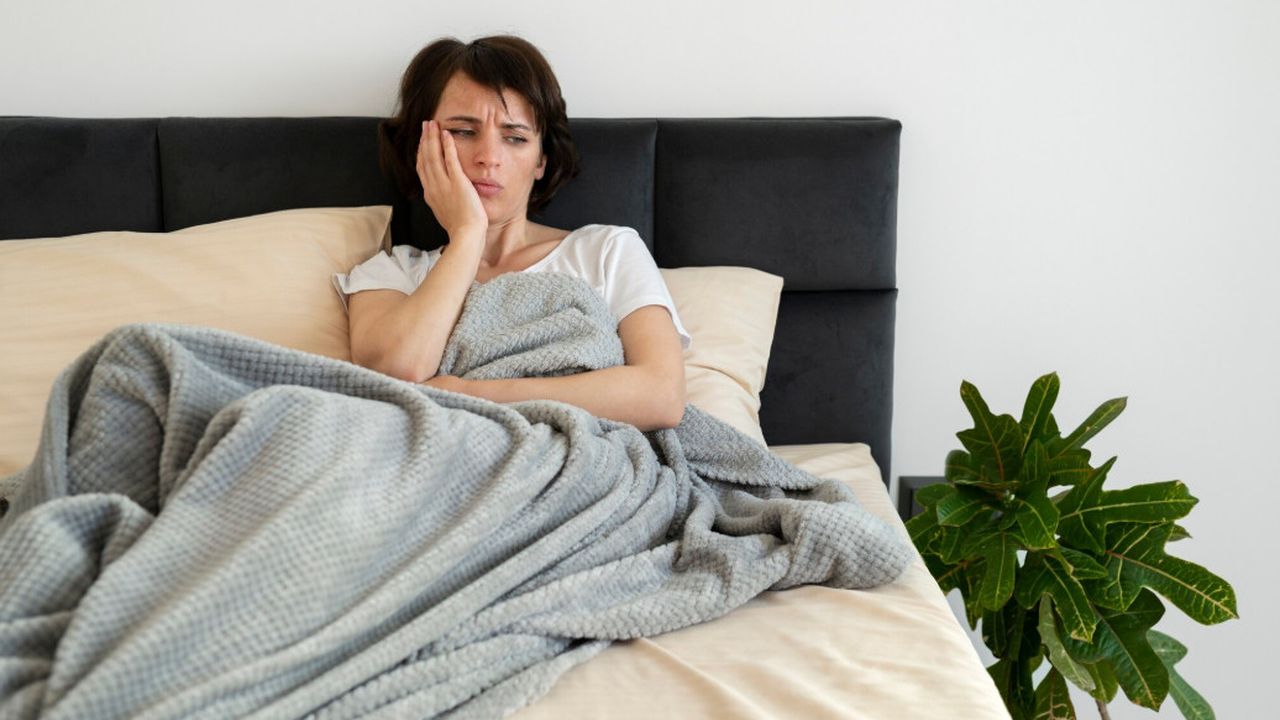 Mulher deitada na cama, aparentemente com problemas de sono, segurando o rosto