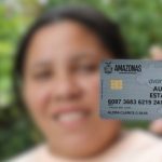 Mulher segurando cartão Auxílio Estadual Amazonas, com aviso sobre uso em apostas.