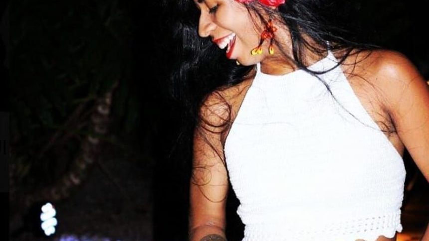 Mulher sorrindo com flores no cabelo e top branco, em evento de música latina.