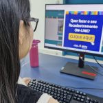Mulher usando computador com aviso sobre recadastramento online.