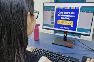 Mulher usando computador com aviso sobre recadastramento online.