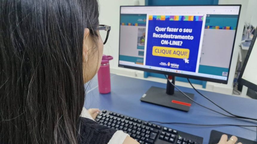 Mulher usando computador com aviso sobre recadastramento online.