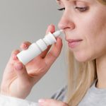 Mulher usando spray nasal para descongestão, seguindo orientações médicas.