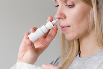 Mulher usando spray nasal para descongestão, seguindo orientações médicas.