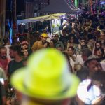 Multidão em festa na rua Barroso, com barracas e luzes coloridas à noite.