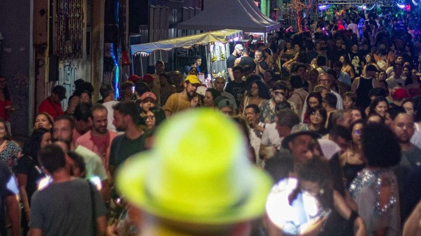 Multidão em festa na rua Barroso, com barracas e luzes coloridas à noite.
