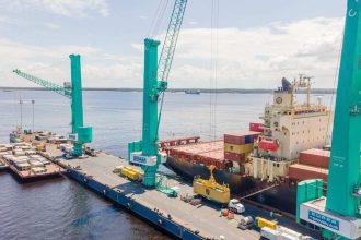 Navio de carga sendo carregado por guindastes no porto de Manaus, com o logo da Super Terminais visível.