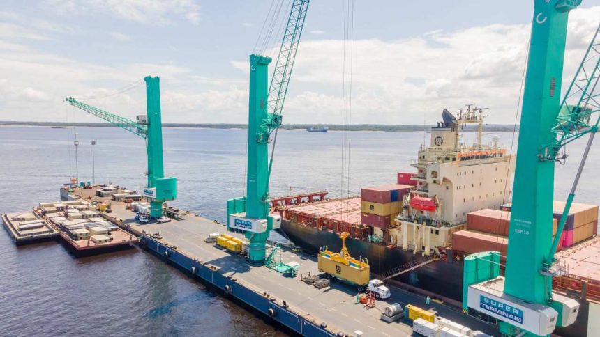 Navio de carga sendo carregado por guindastes no porto de Manaus, com o logo da Super Terminais visível.